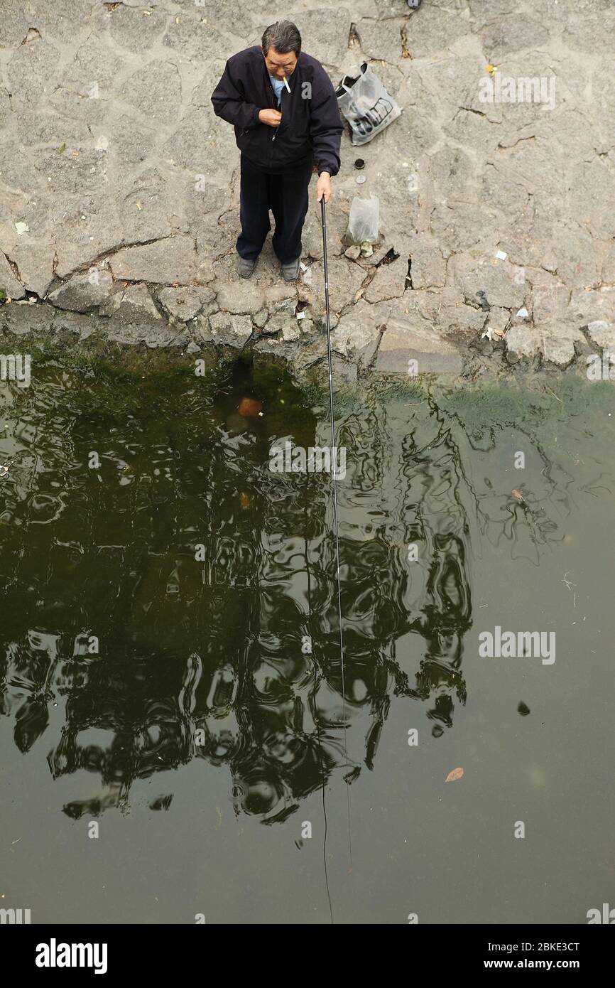 Alter Mann mit einer Zigarette im Mund beim Angeln an einem Kanal. Peking, China Stockfoto