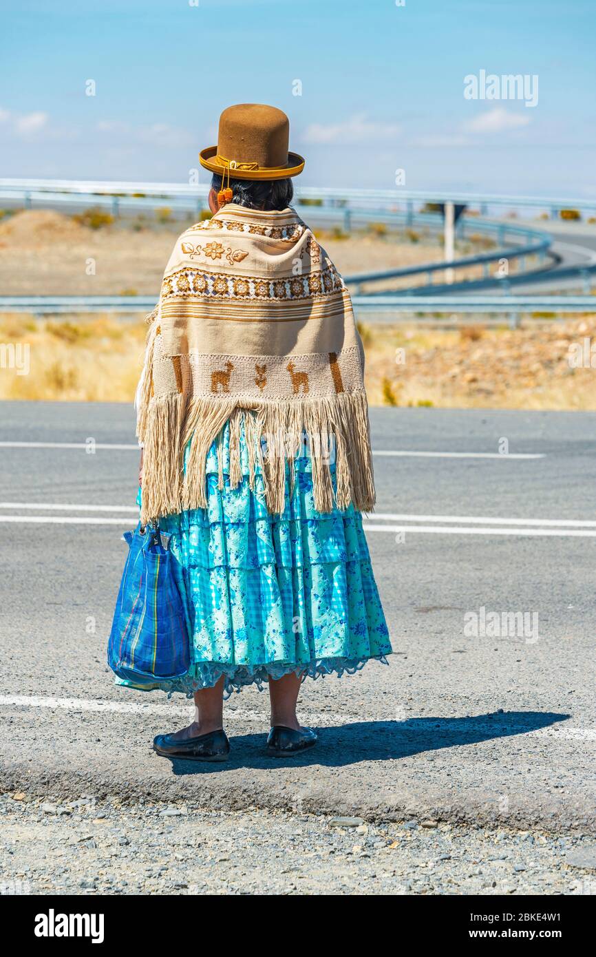 Bolivianische indigene Aymara Frau wartet auf den Transport entlang der Autobahn in traditioneller Kleidung, La Paz, Bolivien. Stockfoto