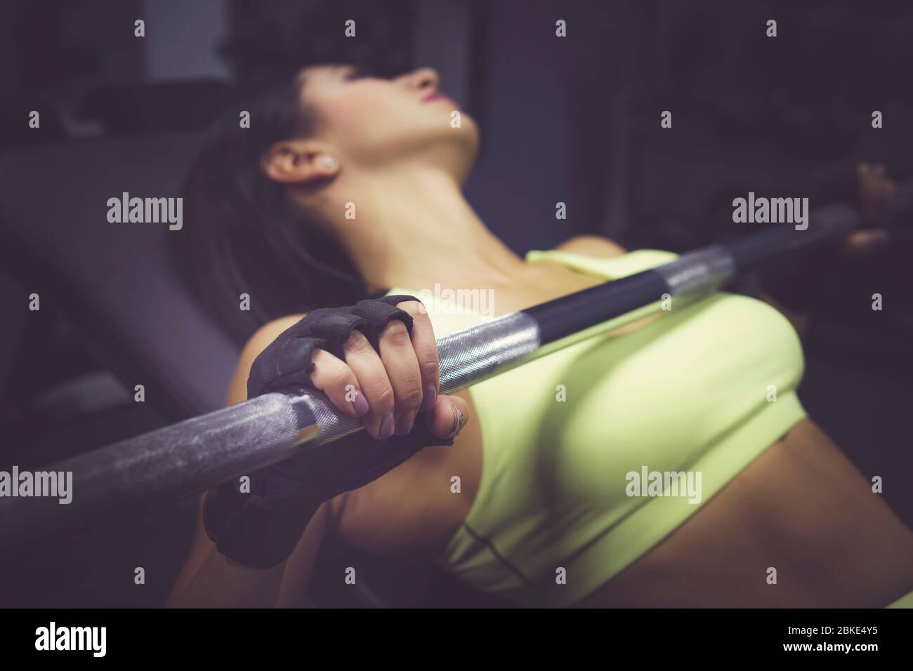 Close up Portrait von sportliche Mädchen Workout auf übung Maschine in der Turnhalle. Schöne Mädchen drücken Barbell in fitness Fitnessraum, dunklen Hintergrund. Sport, bodyb Stockfoto
