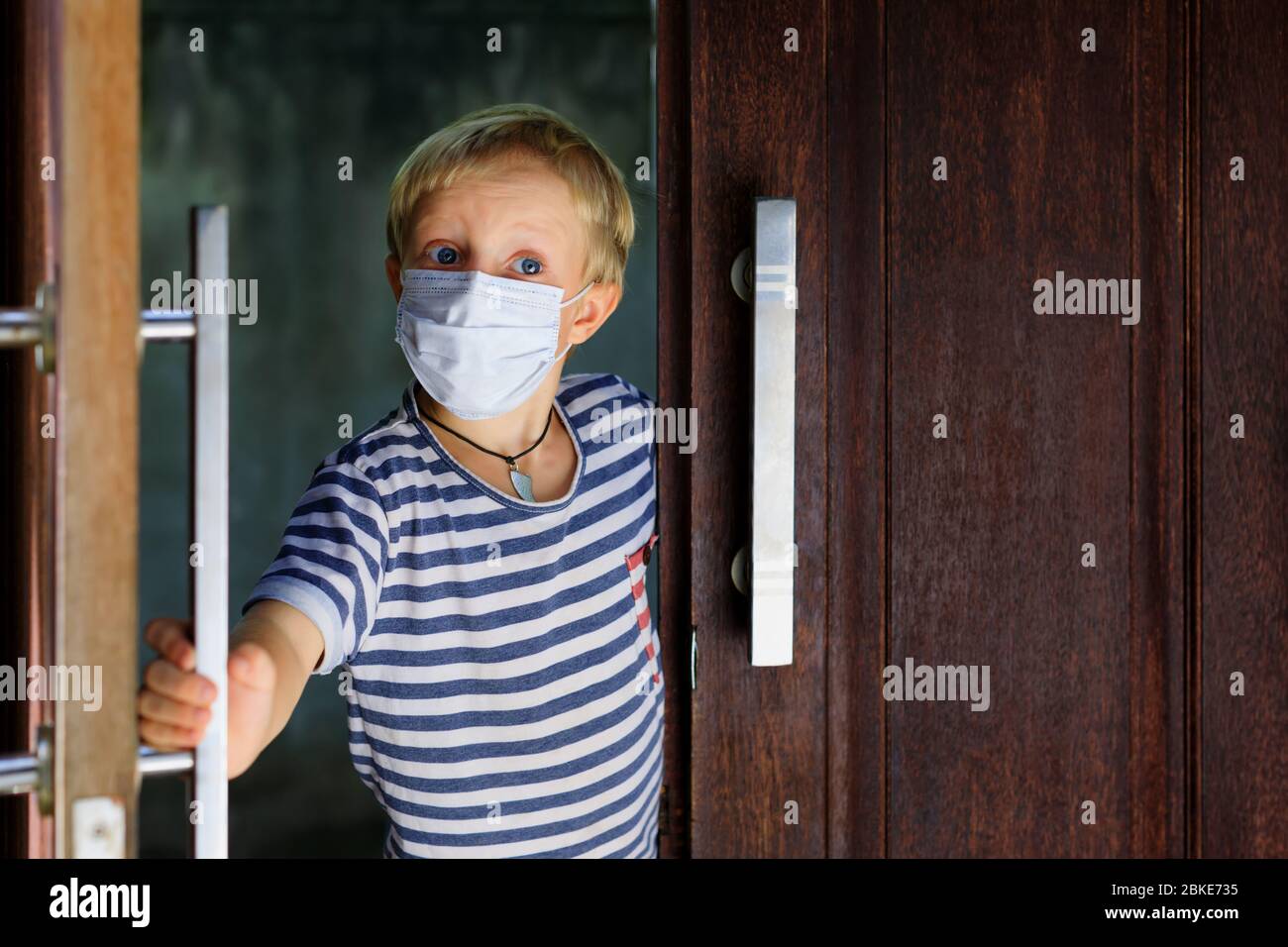 Kleines Kind, das nach dem Aufenthalt zu Hause aus der Tür aufschaute, da es auf der Straße verboten war. Kind trägt medizinische Gesichtsmasken gehen für außerhalb gehen. Stockfoto