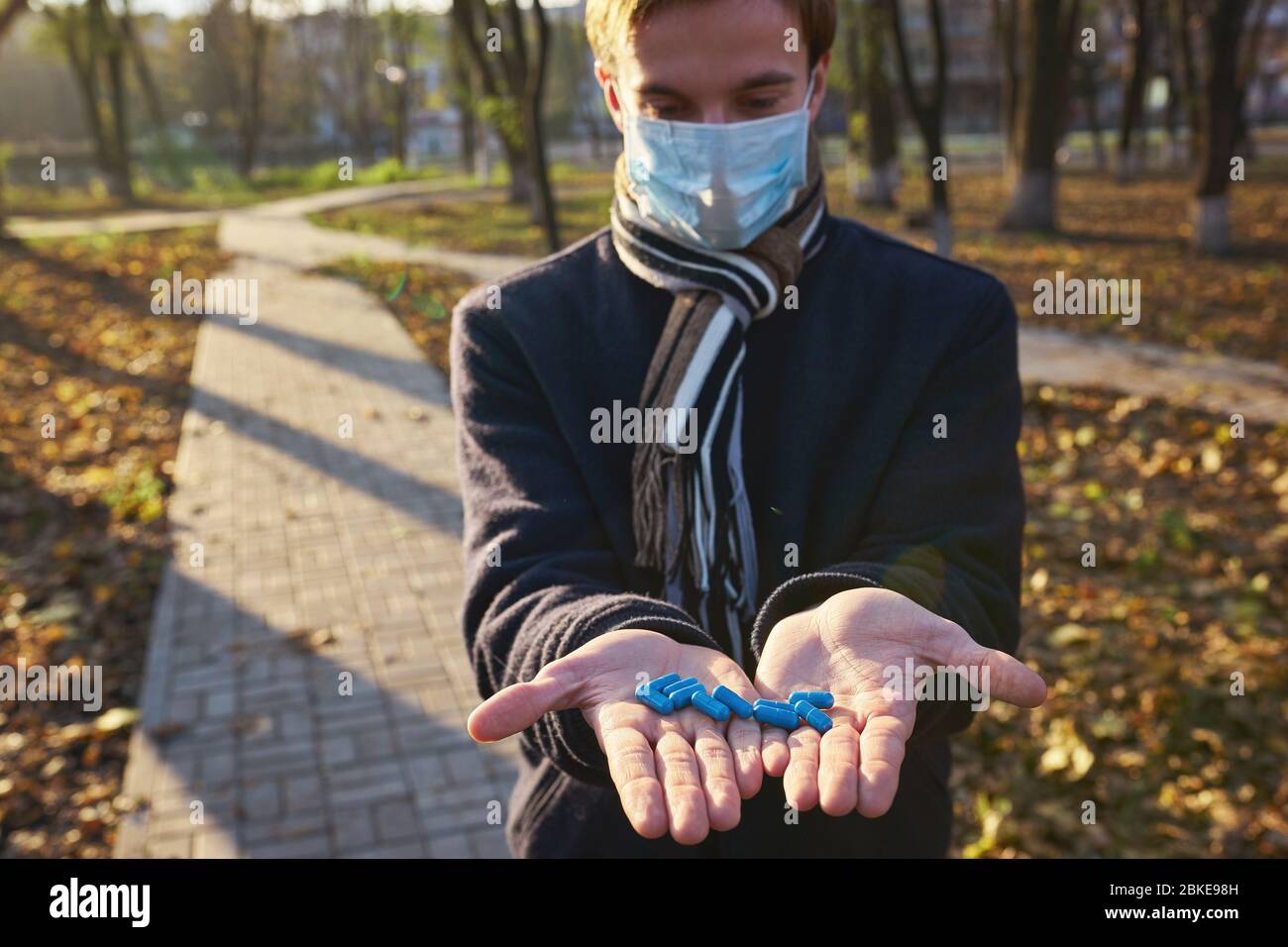 Ein Mann in einer medizinischen Maske hält seine Hände mit Pillen an die Kamera. Konzeptfoto zur Pandemie Covid 19 Stockfoto