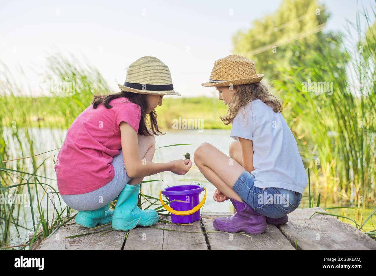 Mädchen sitzen auf Holzpier und fangen Wasserschnecken im Eimer Stockfoto