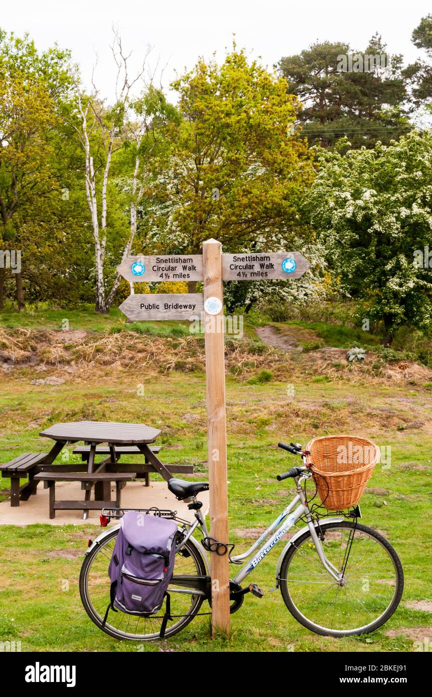Fahrrad gegen eine öffentliche Brücke gelehnt und Rundweg-Wegweiser in Snettisham Common, Norfolk. Stockfoto