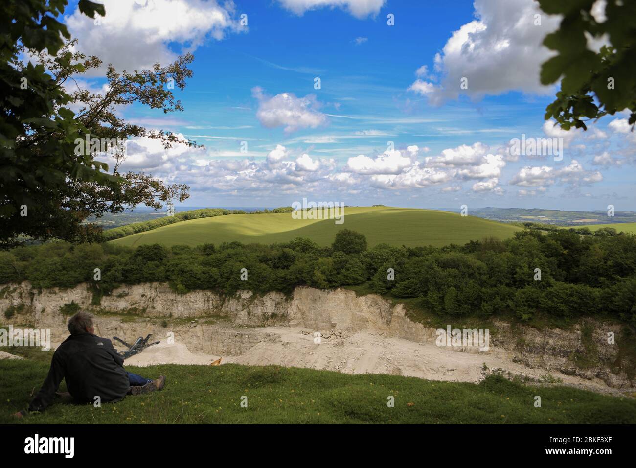 Mann, der sich im Sommersonne entspannt, unter einem Sommerhimmel liegt und seine Augen mit beiden Armen vor der Sonne schützt Stockfoto