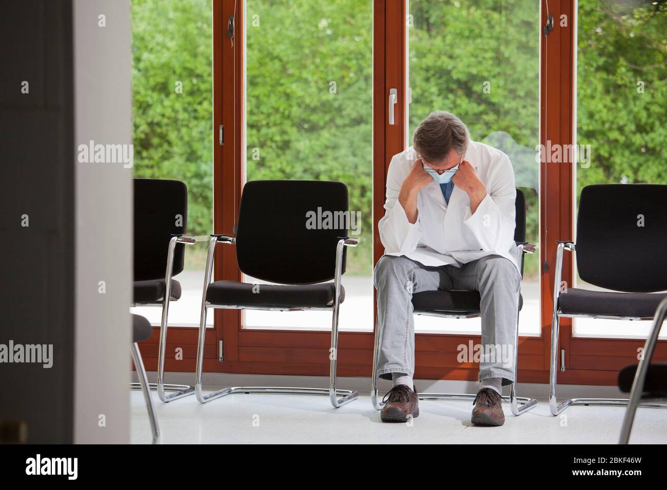 Müde und überarbeiteter Arzt oder Facharzt mit chirurgischer Maske in einem leeren Wartezimmer sitzen Stockfoto