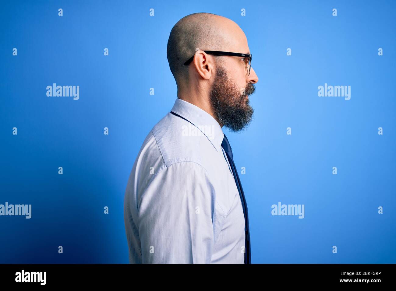 Schöner Geschäft Glatze Mann mit Bart tragen elegante Krawatte und Brille  über blauem Hintergrund suchen zur Seite, entspannen Profil Pose mit  natürlichen Gesicht mit Stockfotografie - Alamy