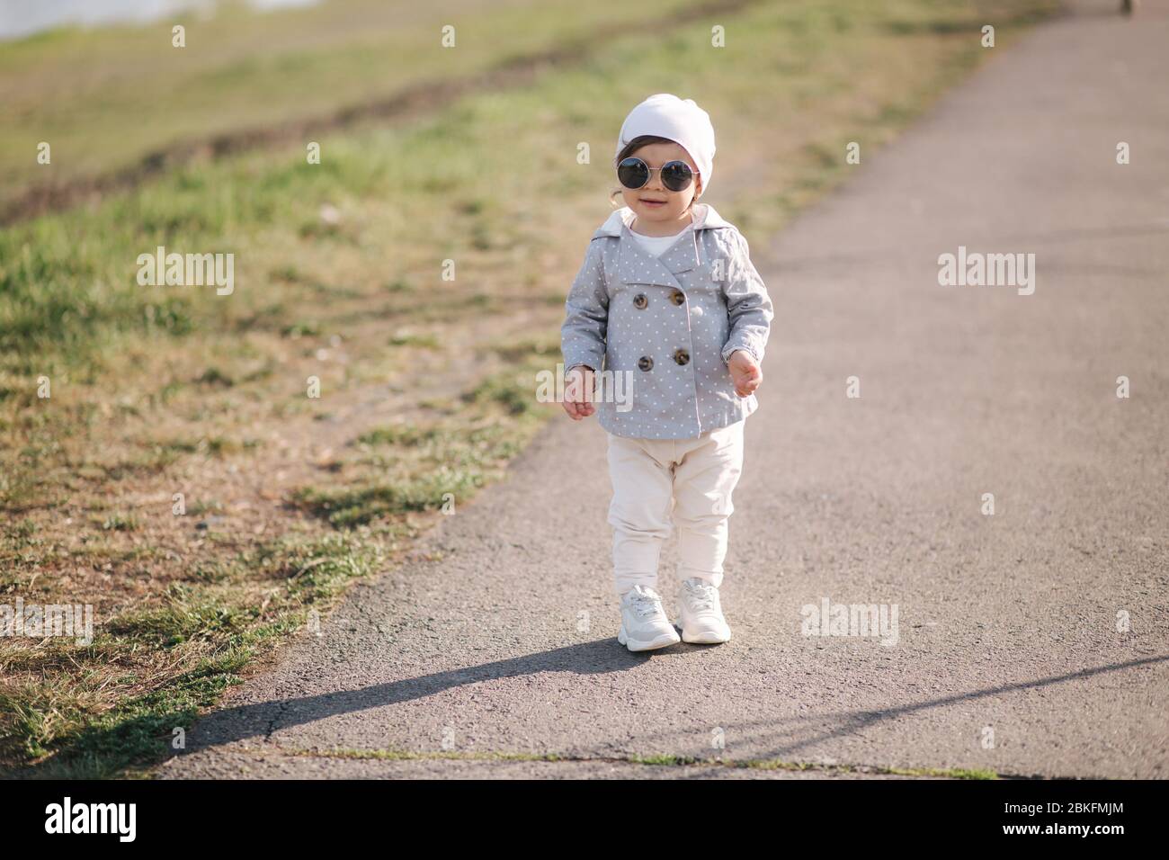 Nettes Mädchen zu Fuß im Park in der Nähe der Böschung. Stilvolle Mädchen in Sonnenbrille Stockfoto