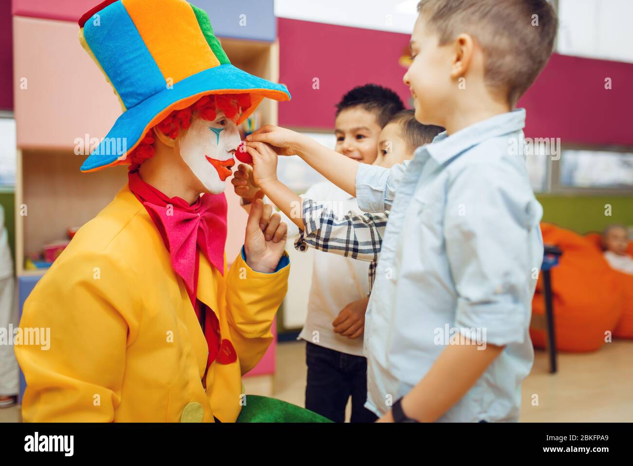 Kleiner fröhlicher Junge berührt die Nase des roten Clowns Stockfoto