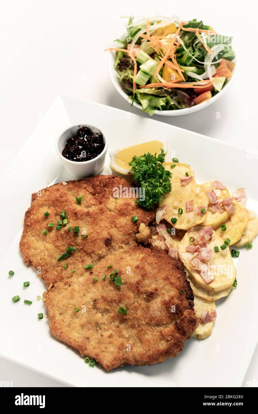 deutsche panierte Schweinefleischschnitzel mit Speck Bratkartoffeln Preiselbeersauce und Salat auf weißem Studiohintergrund Stockfoto