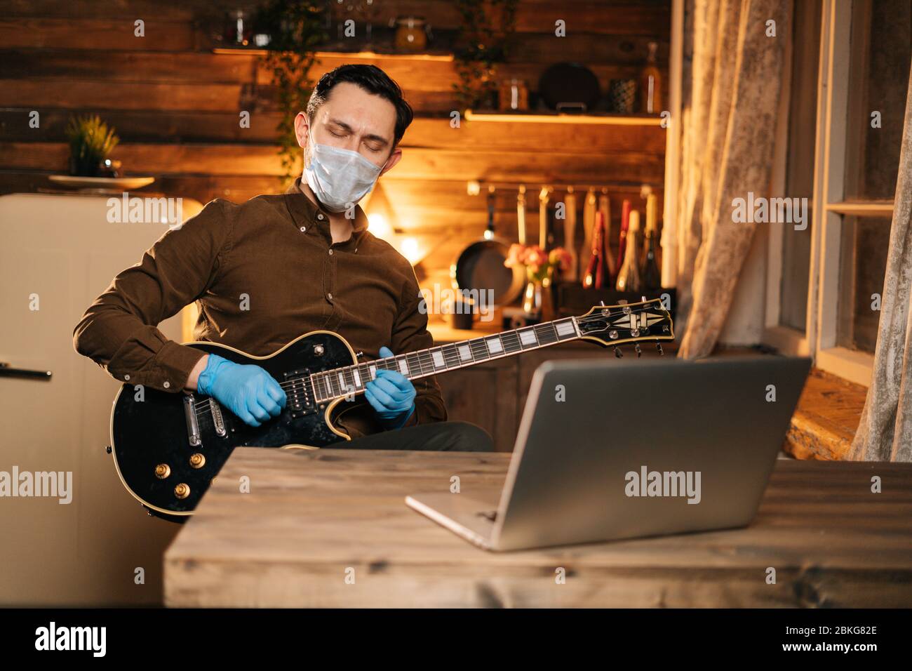 Junger Mann in Maske und Gummihandschuhen spielt Gitarre zu Hause Stockfoto