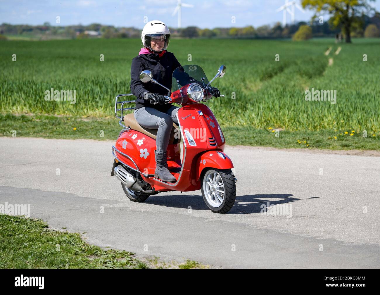 Kiel, Deutschland. Mai 2020. Bei sonnigem Wetter fährt eine Frau mit ihrem roten 125 ccm Vespa Roller auf einer unbefestigten Straße mit Schutzkleidung, Helm und Handschuhen. Seit 01.01.2020 brauchen Inhaber eines Autoführerscheins keinen separaten Motorradführerschein mehr. Nur 5 Fahrstunden und 4 Theoriestunden reichen aus, um Zweiräder bis zu 125 ccm fahren zu dürfen. Quelle: Axel Heimken/dpa/Alamy Live News Stockfoto