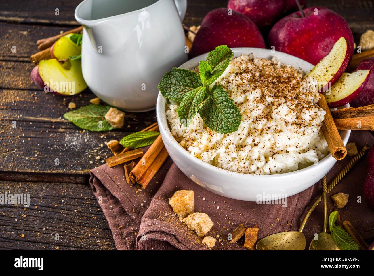 Warmes Herbstfrühstück oder Mittagessen Porridge oder Pudding mit Apfel und Gewürzen. Reisbrei mit Zimt und roten Äpfeln, auf rustikalem Holzhintergrund. Stockfoto