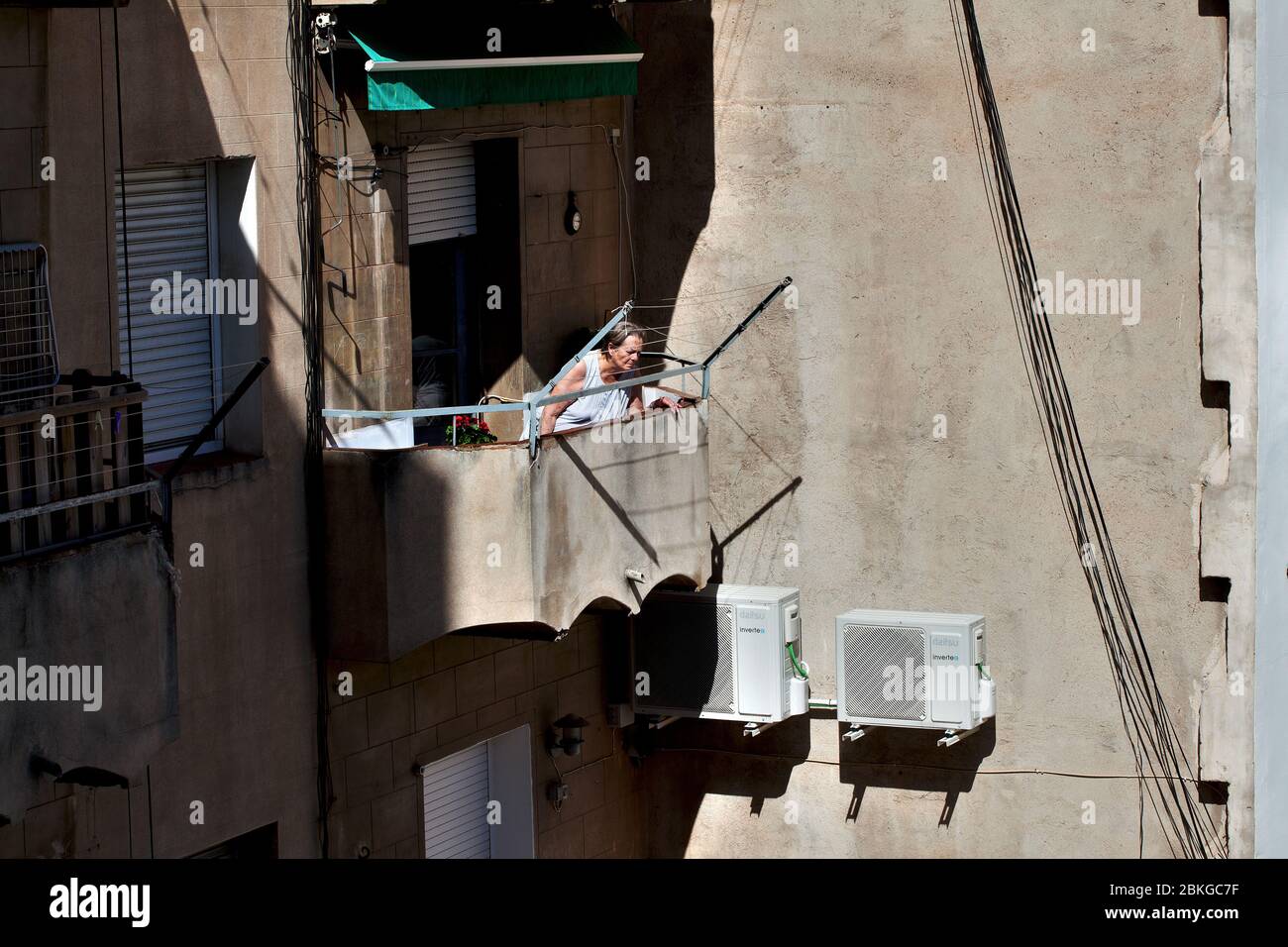 Alte Frau schaut sich die Nachbarin unten an, während sie sich auf ihrem Balkon sonnen, während Lockdown ein wenig lockern wird. Stockfoto