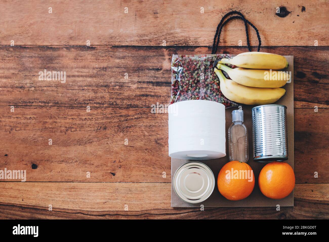 Papiertüte mit Lebensmitteln, Toilettenpapier und Handdesinfektionsmittel darauf. Flach auf dem Holztisch liegen. Flach auf dem Holztisch liegen. Covid-19 Ausbruch, Selbstisolierung, Lieferung, Spendenkonzept. Stockfoto