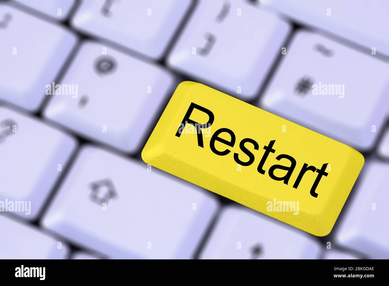 Eine Tastatur mit dem Wort RESTART auf einer gelben ENTER-Taste auf einem verschwommenen Hintergrund der Tasten. England, Großbritannien Stockfoto