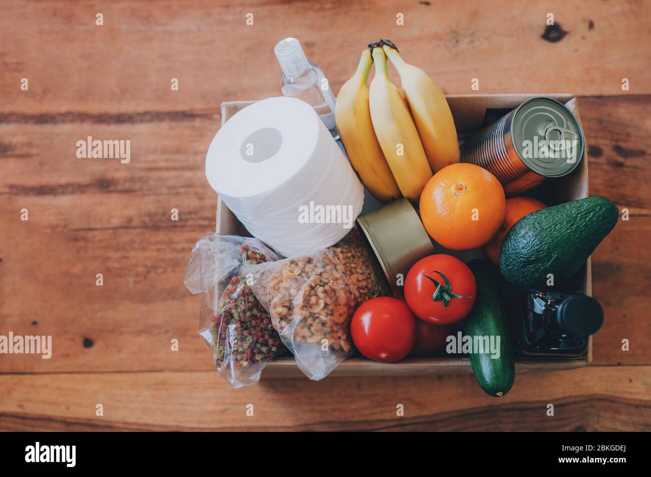 Box mit Lebensmitteln, Toilettenpapier und Handdesinfektionsmittel auf dem Holztisch. Flaches Lay. Covid-19 Ausbruch, Selbstisolierung, Lieferung, Spendenkonzept. Stockfoto