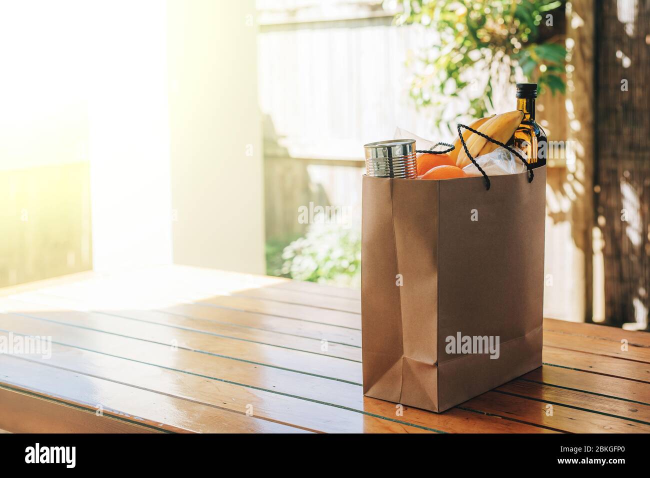 Papiertüte mit Essen auf dem Holztisch im Hinterhof eines Hauses. Covid-19 Ausbruch, Selbstisolierung, Lieferung, Spende. Stockfoto