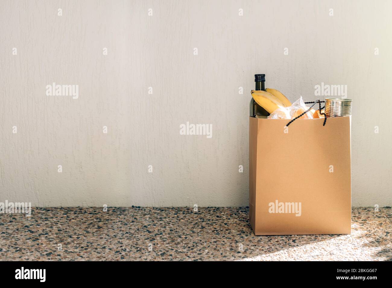 Papiertüte mit Lebensmitteln auf dem Boden neben der Hauswand. Covid-19 Ausbruch, Selbstisolierung, Lieferung, Spende. Stockfoto