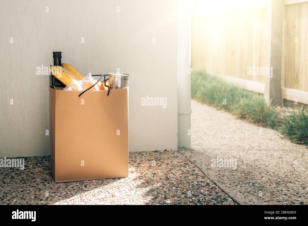 Papiertüte mit Lebensmitteln auf dem Boden neben der Hauswand. Covid-19 Ausbruch, Selbstisolierung, Lieferung, Spende. Stockfoto
