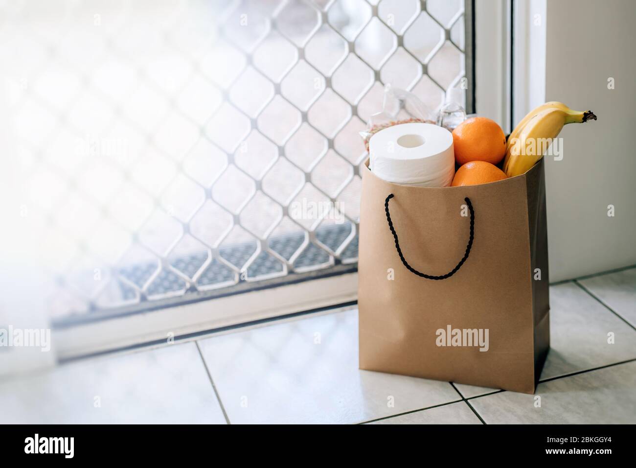 Papiertüte mit Essen und Toilettenpapier auf dem Boden am Eingang zum Haus. Covid-19 Ausbruch, Selbstisolierung, Lieferung, Spende. Stockfoto