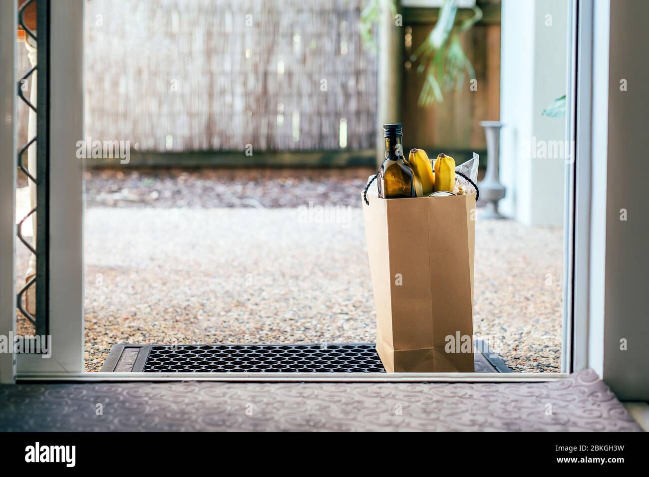 Papiertüte mit Essen und Toilettenpapier auf dem Boden am Eingang zum Haus. Covid-19 Ausbruch, Selbstisolierung, Lieferung, Spende. Stockfoto