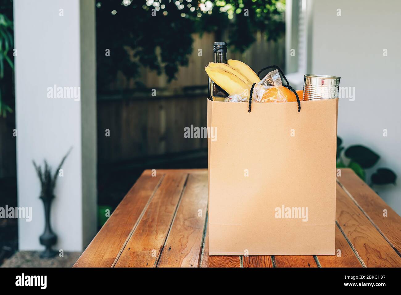 Papiertüte mit Essen auf dem Holztisch im Hinterhof eines Hauses. Covid-19 Ausbruch, Selbstisolierung, Lieferung, Spende. Stockfoto