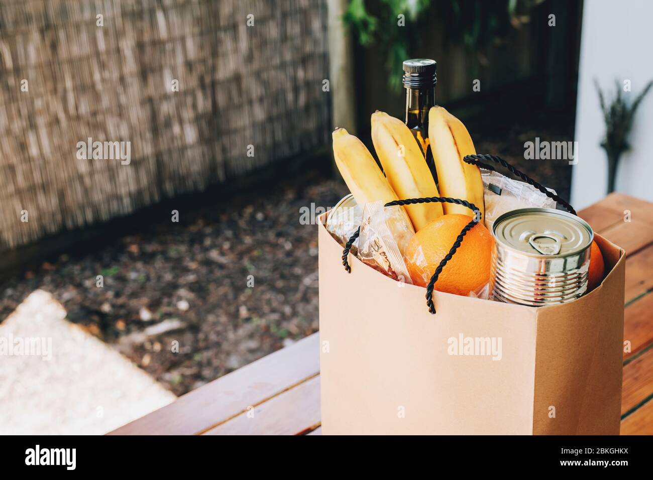 Papiertüte mit Essen auf dem Holztisch im Hinterhof eines Hauses. Covid-19 Ausbruch, Selbstisolierung, Lieferung, Spende. Stockfoto