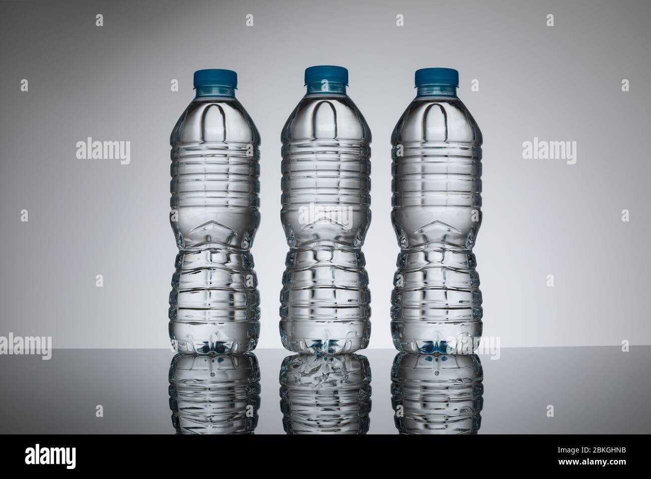 Klare Wasserflaschen aus Kunststoff ohne Etiketten in einer Reihe vor einem schlichten, neutralen Hintergrund. Einzelflaschenversion verfügbar Bild-ID: 2BKGH Stockfoto