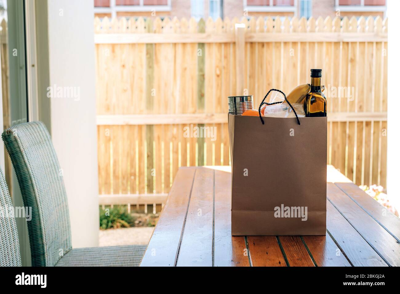 Papiertüte mit Essen auf dem Holztisch im Hinterhof eines Hauses. Covid-19 Ausbruch, Selbstisolierung, Lieferung, Spende. Stockfoto