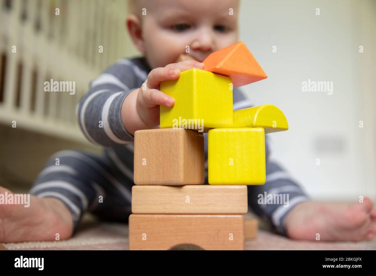 Ein 7 Monate altes Baby, das über einen Stapel hölzerner Spielblöcke schiebt Stockfoto