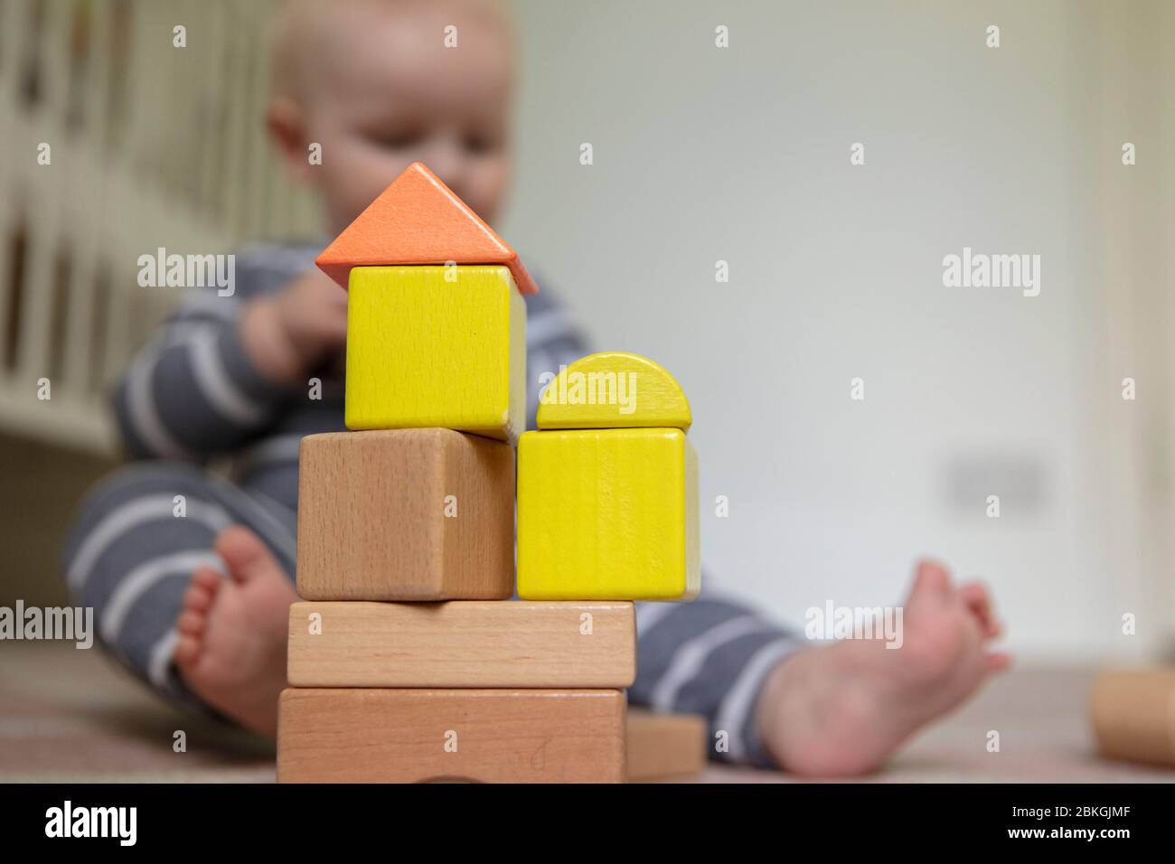 Ein Baby, das mit einem Stapel von bunten hölzernen Spielblöcken in ihrer Kinderstube spielt Stockfoto