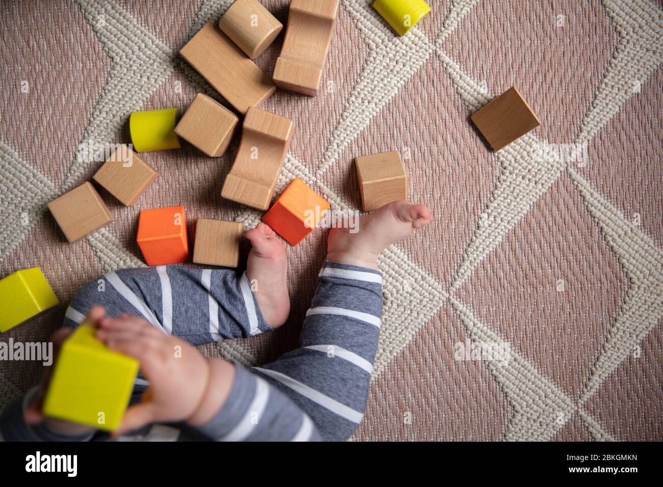 Auf die Beine eines Babys schauend, während sie mit hellen Holzbausteinen spielen Stockfoto