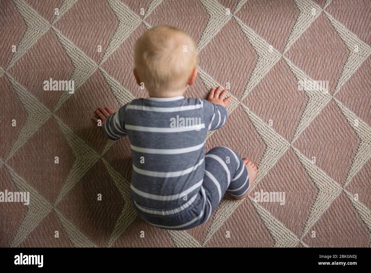 Ein Blick von oben nach unten auf ein süßes Baby, das versucht, auf einem Teppich zu kriechen Stockfoto