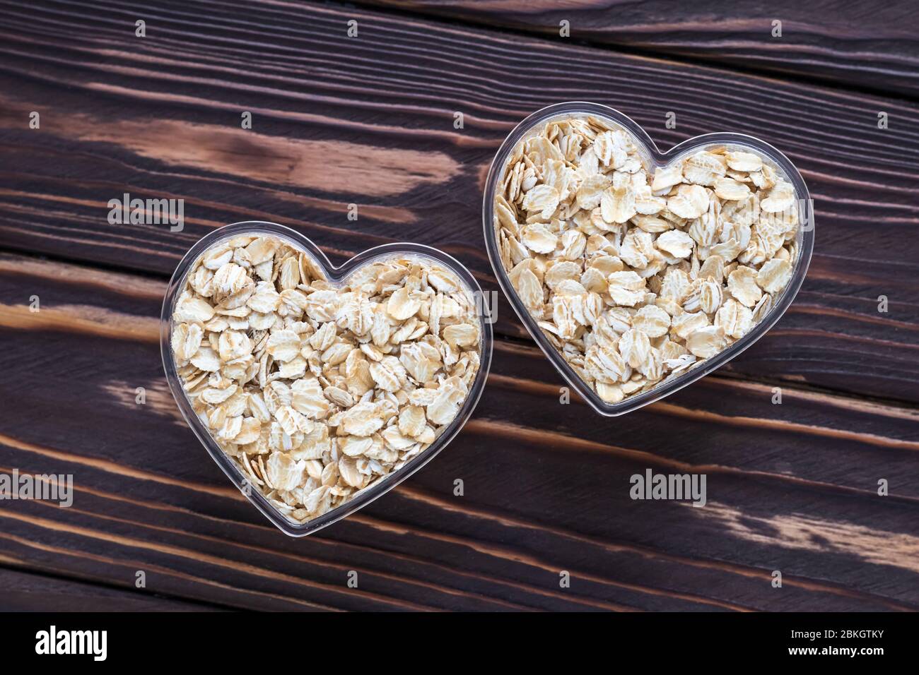 Rohe Haferflocken auf dunklem Holzbrett Hintergrund. Trocknen Sie rohe Cerealien in zwei Schüssel in Herzform Stockfoto