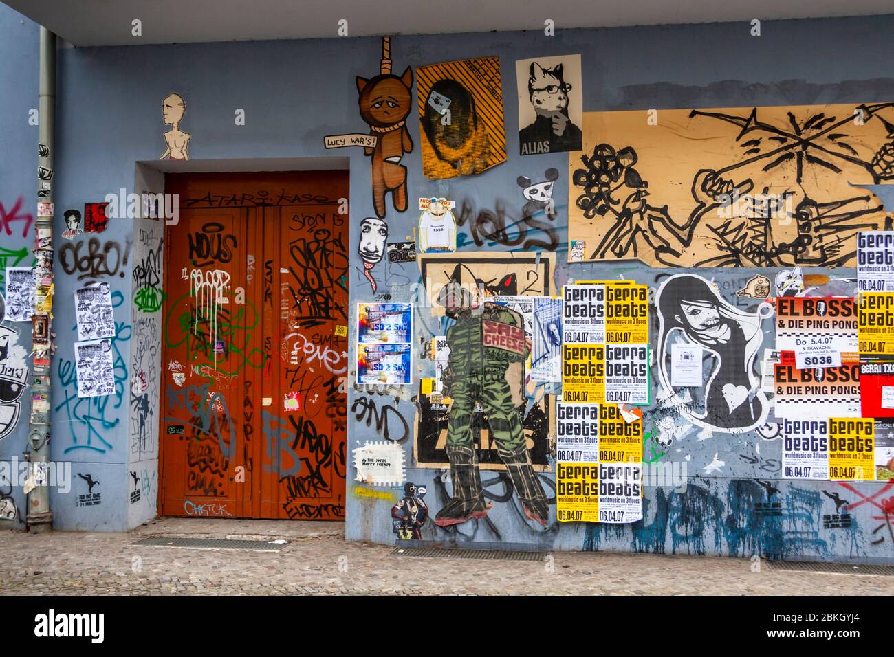 Eine orangefarbene Tür ist von oben bis unten mit Konzertplakaten, Graffiti-Figuren und Aufklebern bedeckt; mehrere Plakate werben für die Partyreihe ‚Terra Beats‘. Boxhagener Straße, Boxhagener Kiez, Friedrichshain, Friedrichshain-Kreuzberg, Berlin, 10245, Deutschland Stockfoto