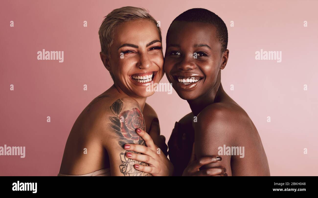 Glücklich diverse weibliche Modelle Blick auf Kamera. Zwei Frauen stehen zusammen und lächeln auf beigefarbenem Hintergrund. Stockfoto