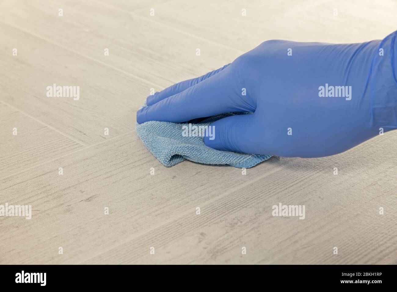 Hand mit blauem Gummihandschuh, um einen Boden mit einem Wischkissen zu reinigen Stockfoto