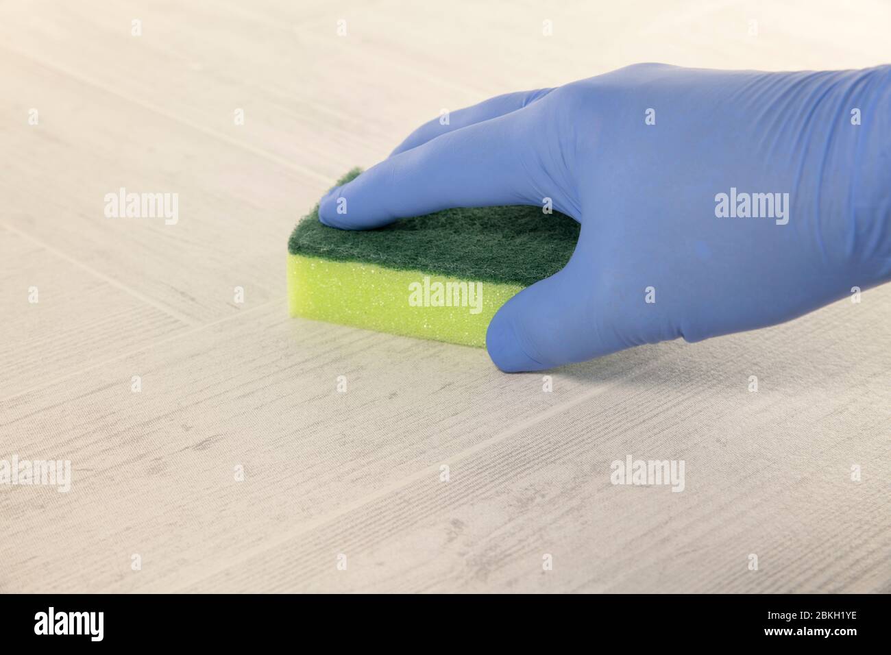 Hand mit blauem Gummihandschuh, um einen Boden mit einem grünen und gelben Reinigungswerkzeug zu reinigen Stockfoto