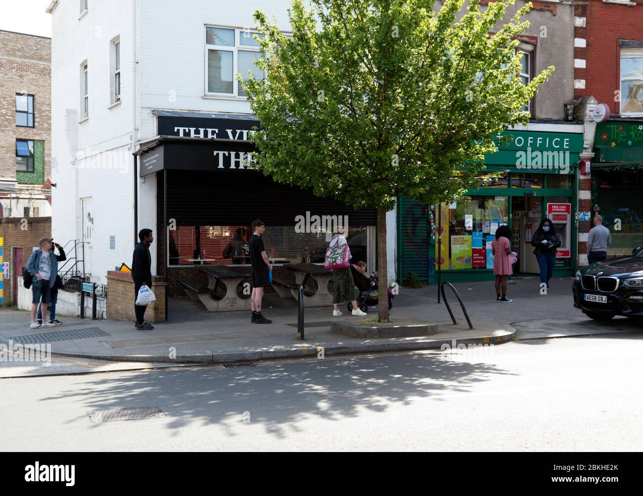 Während der COVID-19 Pandemie beobachten Menschen strenge soziale Distanzierungen, während sie sich anstellen, um das Ladywell Post Office zu betreten Stockfoto