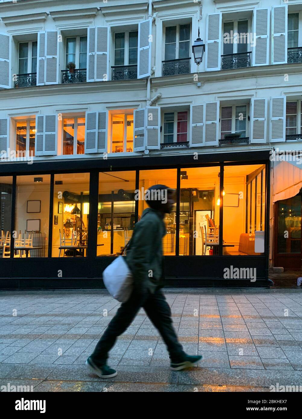 Blick auf den jungen Mann, der vor dem Restaurant und dem historischen, typischen Gebäude am frühen Morgen in Paris läuft. Lifestyle- und Kulturkonzept. Stockfoto