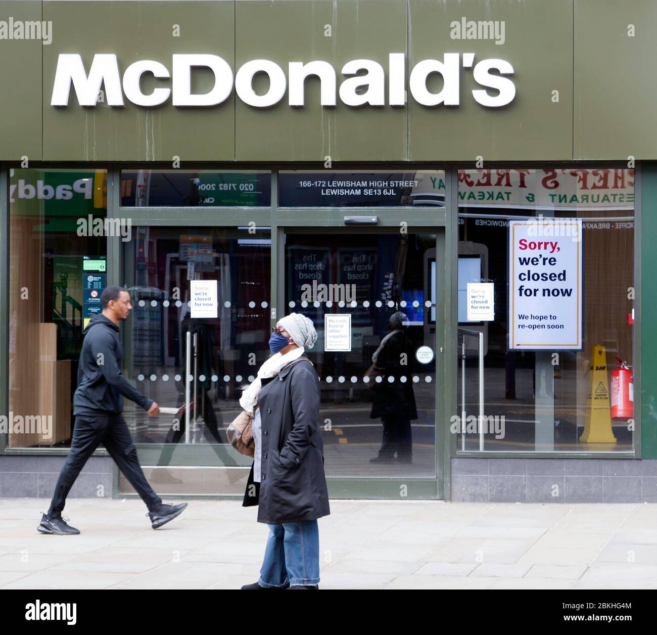 Frau in einer Gesichtsmaske geht während der COVID-19 Pandemie vor einem geschlossenen McDonalds Outlet, in der Lewisham High Street, vorbei. Stockfoto