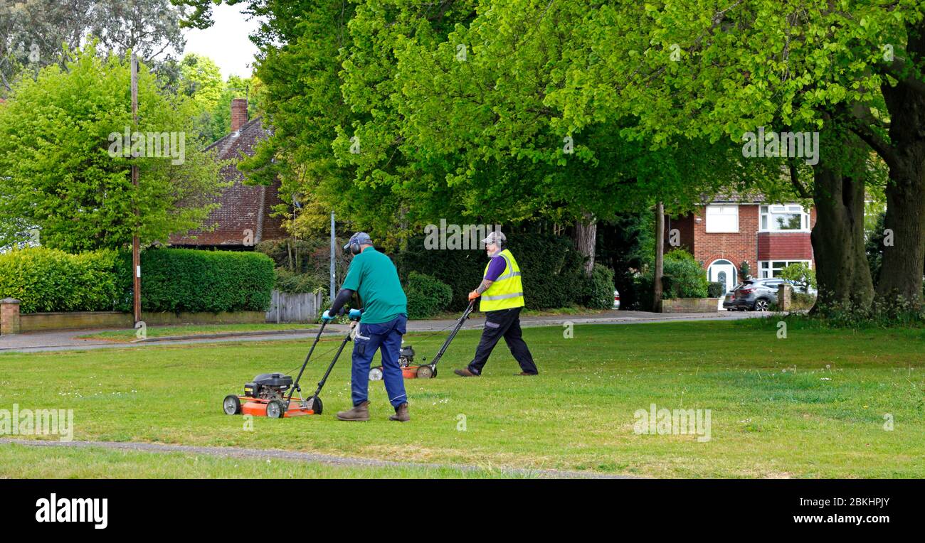 Zwei Männer, die auf einem kleinen Grün in einem Wohngebiet in Hellesdon, Norfolk, England, Großbritannien, Gras schneiden. Stockfoto