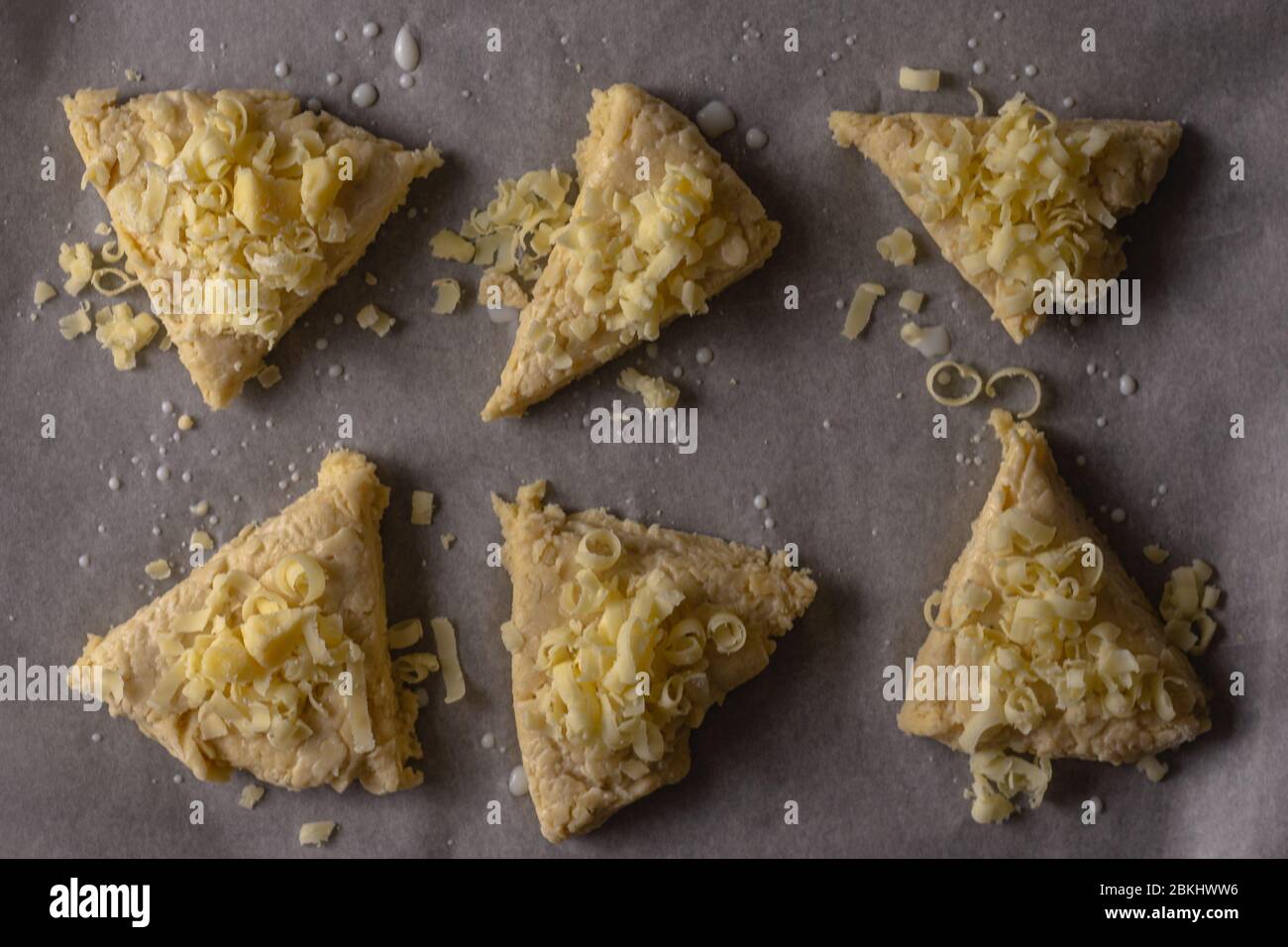 Ein Blick auf rohe Käseschaufeln von oben nach unten. Die Scones wurden in Dreiecke geschnitten und mit geriebenem Käse überstanzt Stockfoto