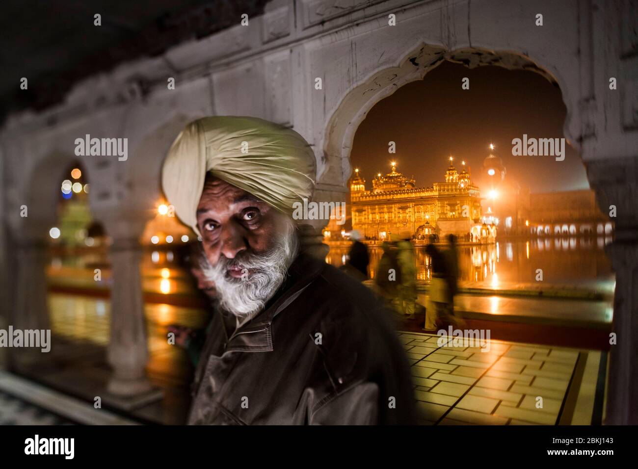 Indien, Punjab Staat, Amritsar, Harmandir Sahib, Porträt eines Sikh-Mannes mit intensiven Augen und Golden Temple beleuchtet in der Nacht im Hintergrund, heiliger Ort des Sikhismus Stockfoto