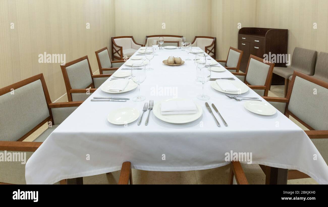 Großer Tisch mit weißer Tischdecke, Tellern und Besteck Stockfoto