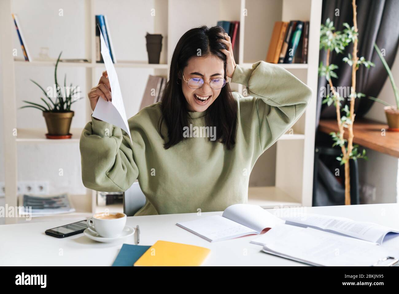 Attraktive müde aufgeregt junge Studentin Studium an der College-Bibliothek, sitzen am Schreibtisch, immer bereit für Prüfungen Stockfoto