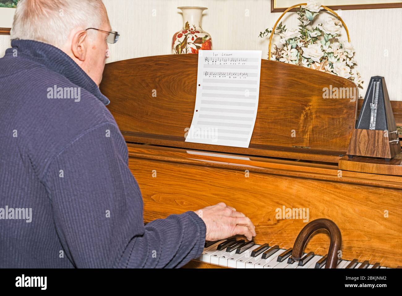Älterer Mann sitzt am Klavier und Spazierstock, der erste Klavierstunde hat. Konzept: Altersaktivität, Stimulation, Lernen, nie zu alt, jung halten. Stockfoto