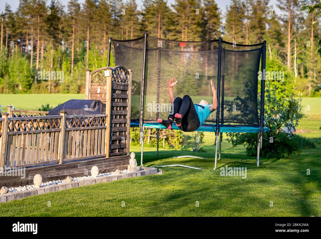 Junge gut ausgebildete sportliche Teenager führt akrobatische Übung salto - Flip rückwärts, Füße und Hände in der Luft. Übung auf grünem Gras in der Nähe von Holzterr Stockfoto