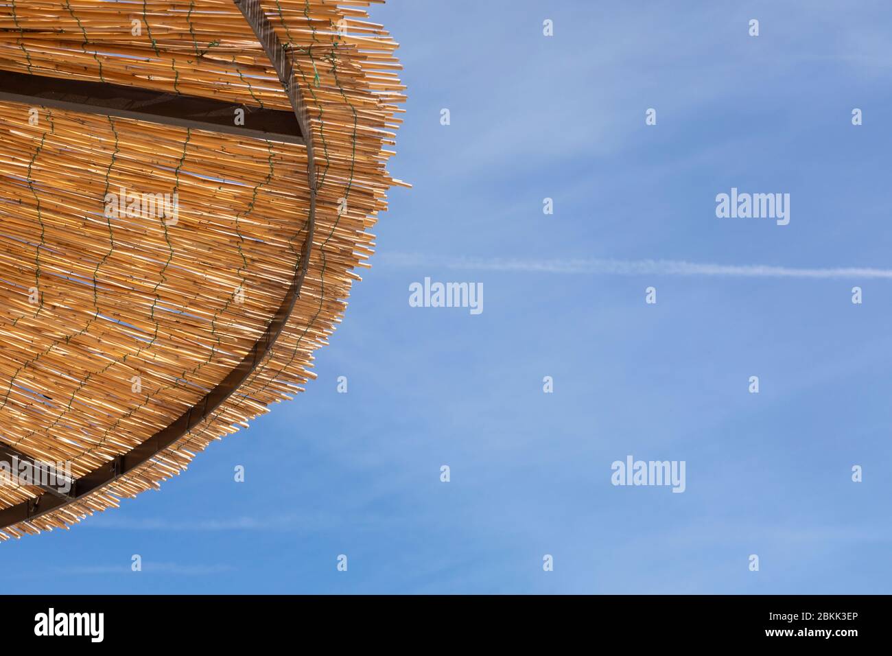Detail eines Strohhalm Sonnenschirm mit Stroh-Details, mit natürlichen Materialien, die Schatten von der Sonne. Ein sonniger Tag im Sommer mit einem blauen Stockfoto