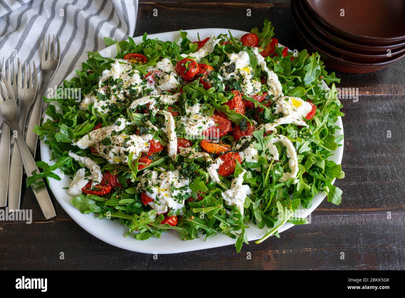 Rucola mit langsam gerösteten Tomaten und Burrata: Eine andere Version des klassischen Caprese-Salats aus Traubentomaten, Rucola, Basilikum und Mozzarella Stockfoto